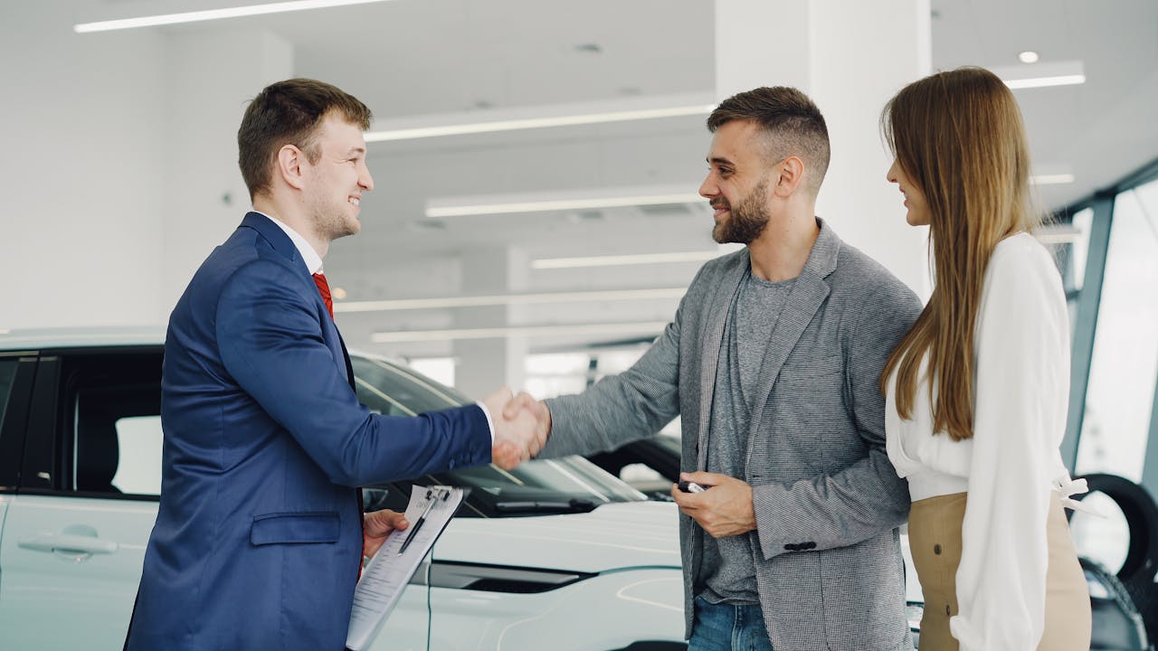 Friendly handshake between a car salesman and customers in a modern car showroom.